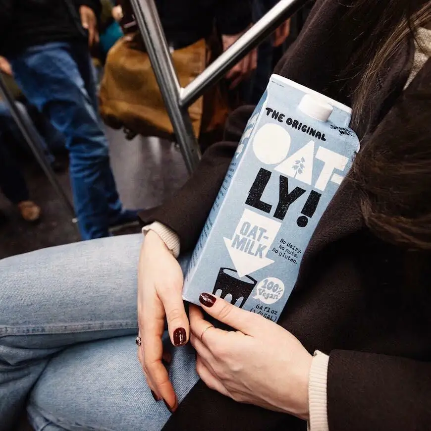 A box of Oatly in the hand of a women sitting down.